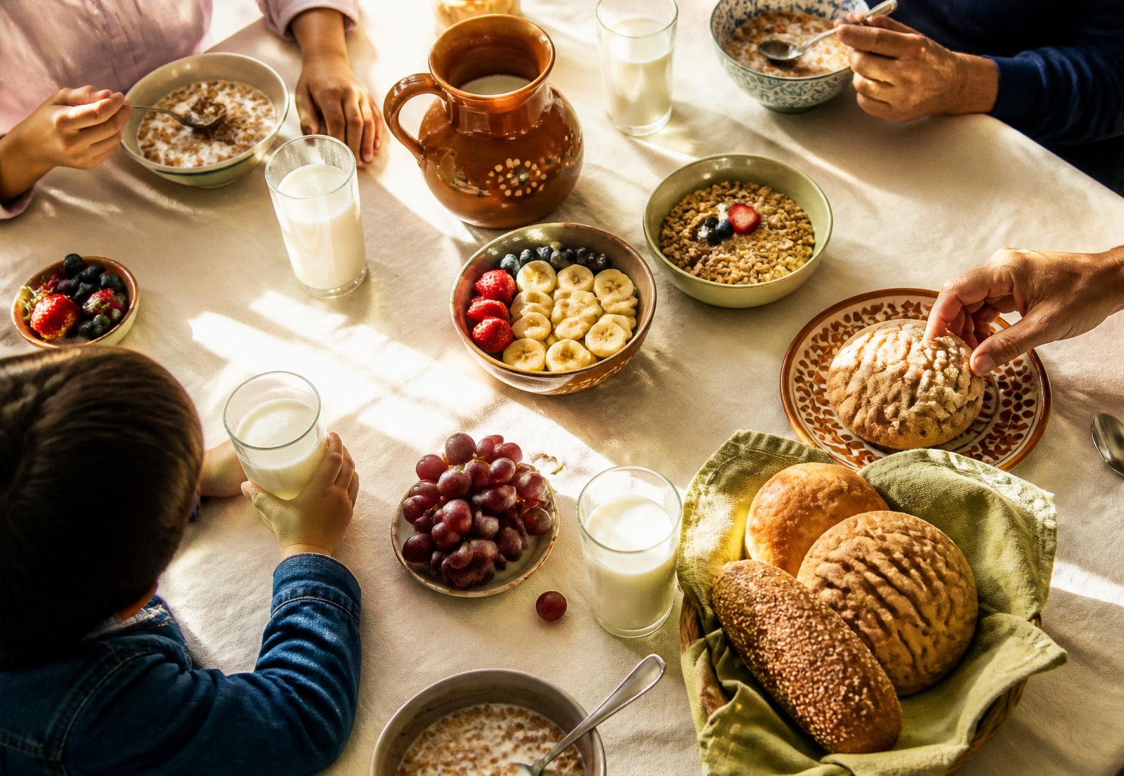 A warm family breakfast table with glasses of Buena milk, fresh fruit, and pan dulce